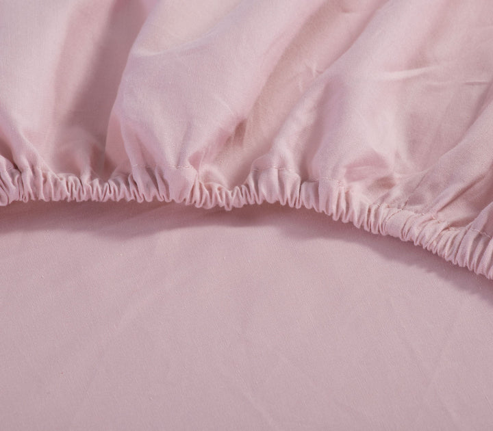 Κοντινή λήψη σε ροζ σεντόνι με λάστιχο, που δείχνει τη λεπτομέρεια της ραφής και της εφαρμογής στη γωνία του στρώματος.