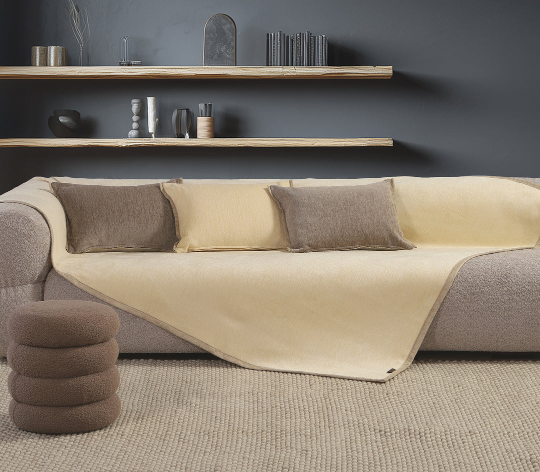 Καναπές διακοσμημένος με εκρού ριχτάρι και καφέ μαξιλάρια σε σαλόνι με σκούρο γκρι τοίχο και ξύλινα ράφια.