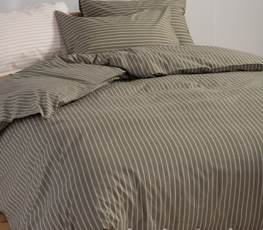 Κρεβάτι με σετ σεντονιών σε πράσινο χρώμα και λευκές ρίγες, διακοσμημένο με μαξιλάρια σε ουδέτερους τόνους.