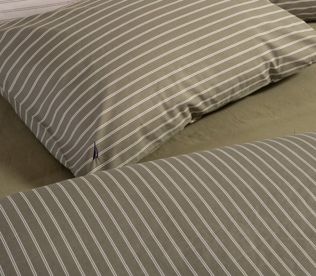 Μαξιλαροθήκη σε πράσινο χρώμα με λευκές κάθετες ρίγες και μικρό κεντητό σχέδιο, τοποθετημένη σε κρεβάτι.