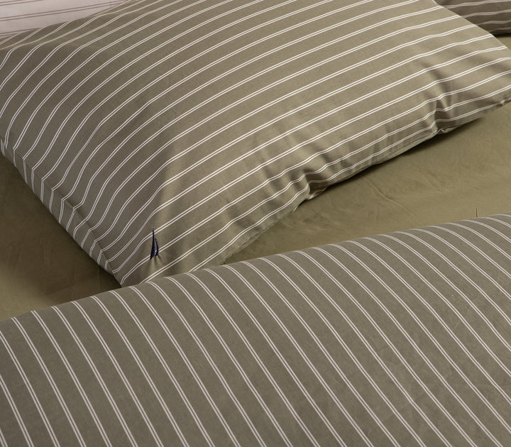 Μαξιλαροθήκη σε πράσινο χρώμα με λευκές κάθετες ρίγες και μικρό κεντητό σχέδιο, τοποθετημένη σε κρεβάτι.