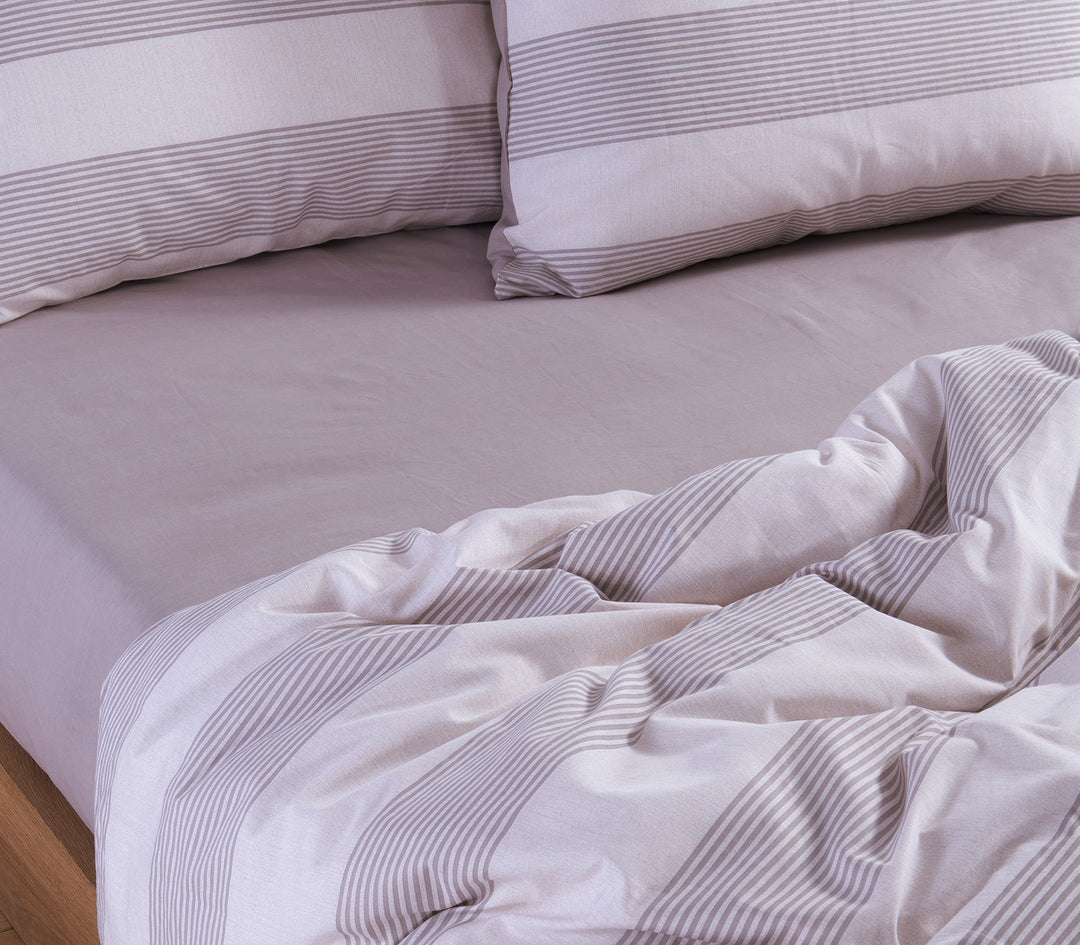 Κρεβάτι με εκρπύ και γκρι ριγέ σεντόνια, με μαξιλάρια στο ίδιο σχέδιο και ένα ελαφρώς ακατάστατο πάπλωμα, δημιουργώντας μια αίσθηση άνεσης και ζεστασιάς.