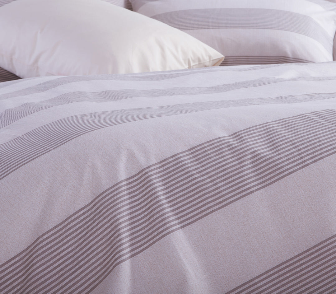 Κοντινό πλάνο από εκρού και γκρι ριγέ πάπλωμα και μαξιλάρια, με έμφαση στην υφή και τις λεπτομέρειες του υφάσματος, αποπνέοντας μια αίσθηση πολυτέλειας και χαλάρωσης.