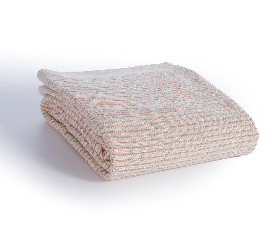 Διπλωμένο ριχτάρι σε ροδακινί χρώμα με οριζόντιες ρίγες και διακριτικό μοτίβο σε παλ ροζ αποχρώσεις.