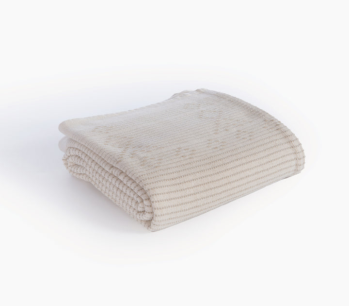 Διπλωμένο ριχτάρι σε μπεζ χρώμα με λεπτές ρίγες και διακριτικό γεωμετρικό σχέδιο.