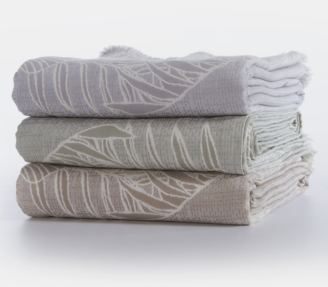 Τρία διπλωμένα ριχτάρια με φυλλωτό σχέδιο, σε γκρι, πράσινη και μπεζ απόχρωση αντίστοιχα.