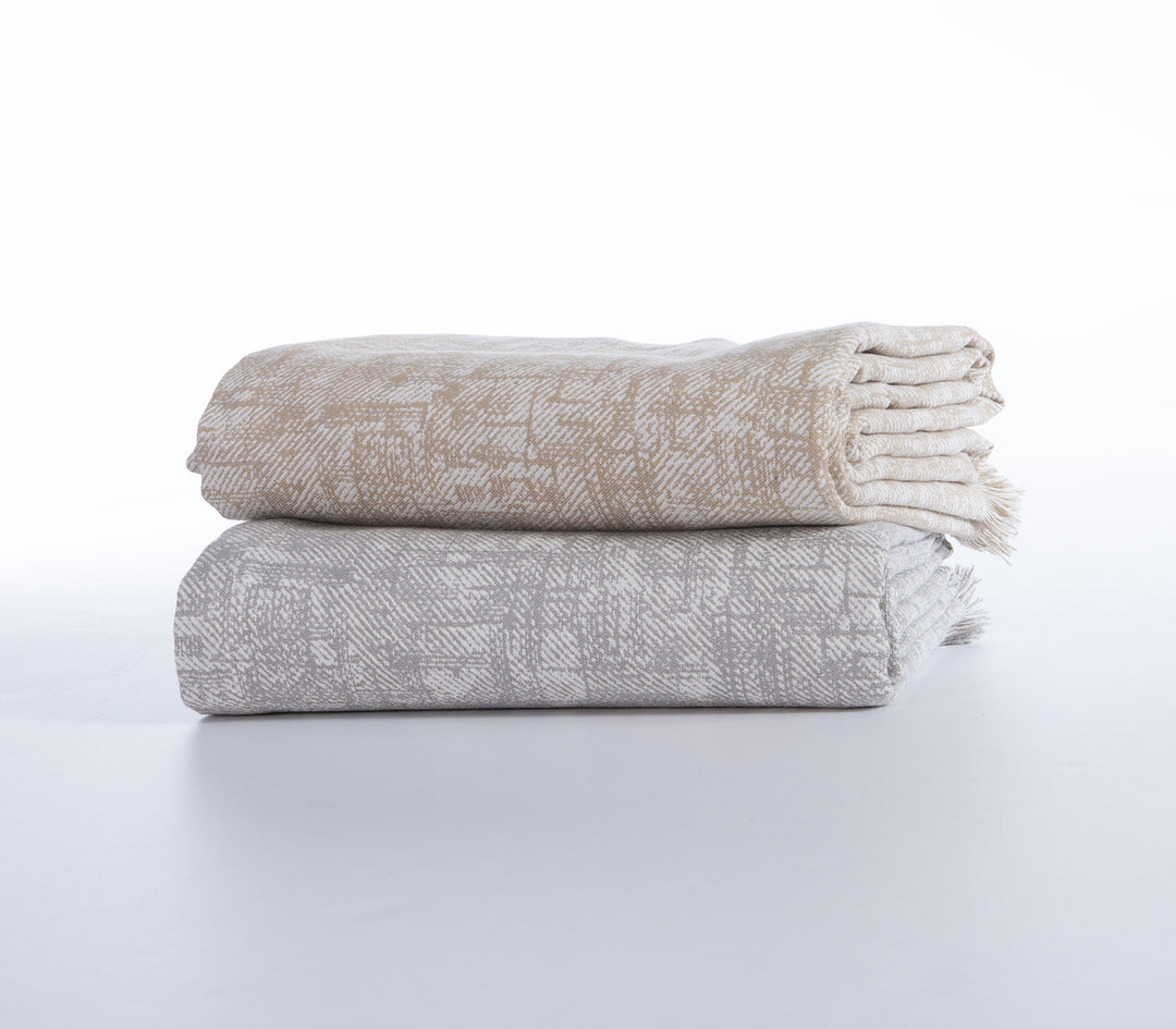 Δύο διπλωμένα ριχτάρια με το ίδιο γεωμετρικό σχέδιο, το ένα σε μπεζ και το άλλο σε γκρι απόχρωση.