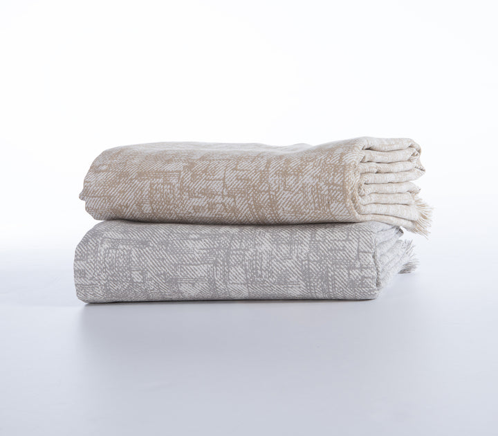 Δύο διπλωμένα ριχτάρια με το ίδιο γεωμετρικό σχέδιο, το ένα σε μπεζ και το άλλο σε γκρι απόχρωση.