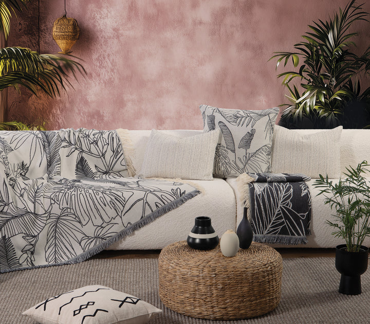 Ριχτάρι σε φυσική απόχρωση με μαύρο τροπικό μοτίβο, στρωμένο σε λευκό καναπέ με αντίστοιχα μαξιλάρια.