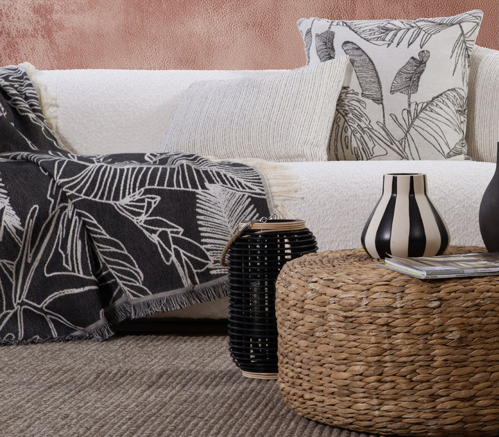 Ριχτάρι σε μαύρο χρώμα με εκρού τροπικό μοτίβο, απλωμένο σε λευκό καναπέ.