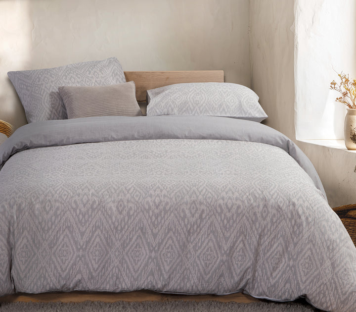 Υπνοδωμάτιο με γκρι σετ σεντόνια γεωμετρικό σχέδιο και διακόσμηση σε φυσικό φως.