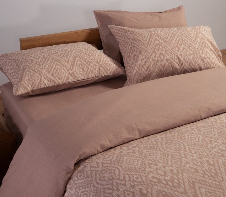 Κρεβάτι στρωμένο με μπεζ σεντόνια γεωμετρικό σχέδιο και μαξιλαροθήκες σε σετ.