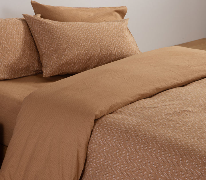 Καφέ σεντόνια με μοτίβο ζιγκ-ζαγκ σε κρεβάτι με ξύλινο πάτωμα.