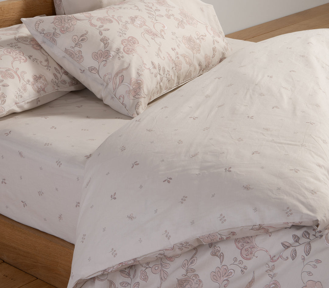 Κρεβάτι στρωμένο με εκρού σετ σεντόνια με διακριτικό ροζ λουλουδάτο μοτίβο.