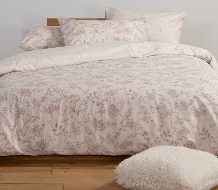 Υπνοδωμάτιο με εκρού σετ σεντόνια με ροζ λουλουδάτο μοτίβο δίπλα σε παράθυρο με φυσικό φως.