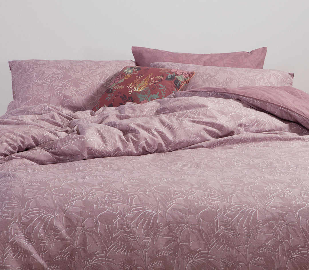 Ροζ σετ σεντόνια με τροπικό μοτίβο φύλλων σε υπνοδωμάτιο με διακόσμηση με λουλουδάτο μαξιλάρι.