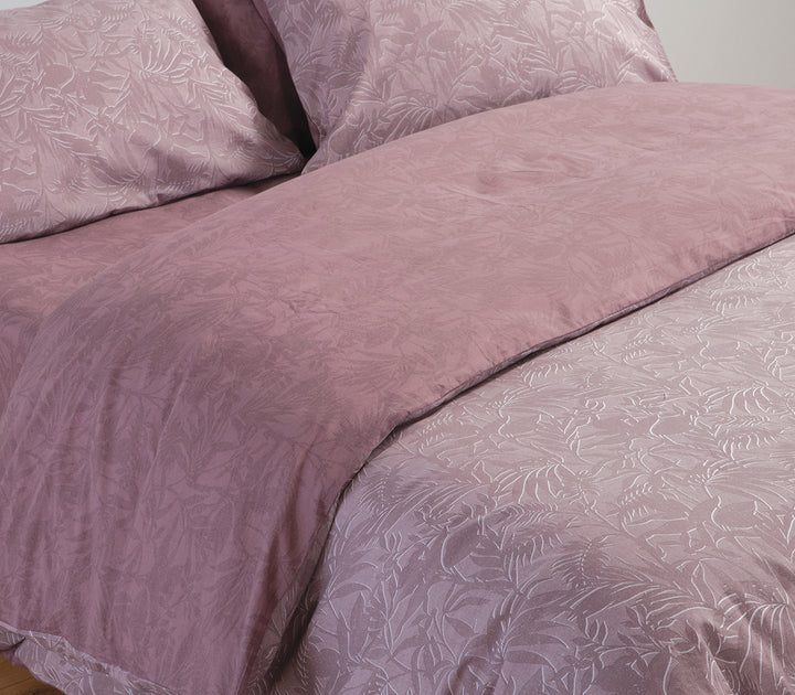 Κρεβάτι με ροζ σετ σεντόνια και μαξιλαροθήκες με τροπικό μοτίβο φύλλων σε κοντινή λήψη.