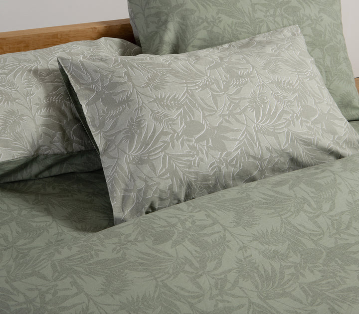 Κρεβάτι με πράσινο σετ σεντόνια και μαξιλαροθήκες με τροπικό σχέδιο φύλλων σε κοντινή λήψη.