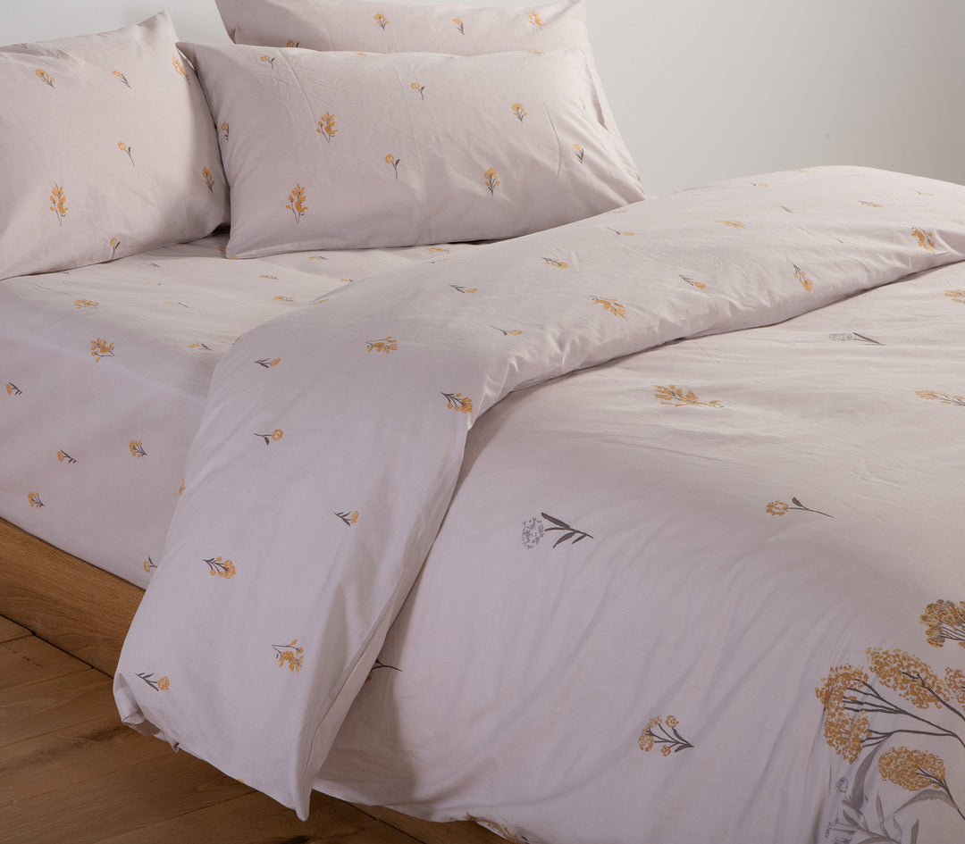 Κοντινή λήψη σε σετ σεντόνια σε απαλό γκρι με κίτρινα λουλούδια κεντημένα, μαξιλαροθήκες και κατωσέντονο.