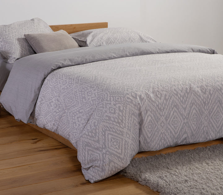 Σετ σεντόνια σε γκρι αποχρώσεις με γεωμετρικά μοτίβα και διακριτική υφή, διακόσμηση με μαξιλάρι σε ουδέτερο χρώμα.