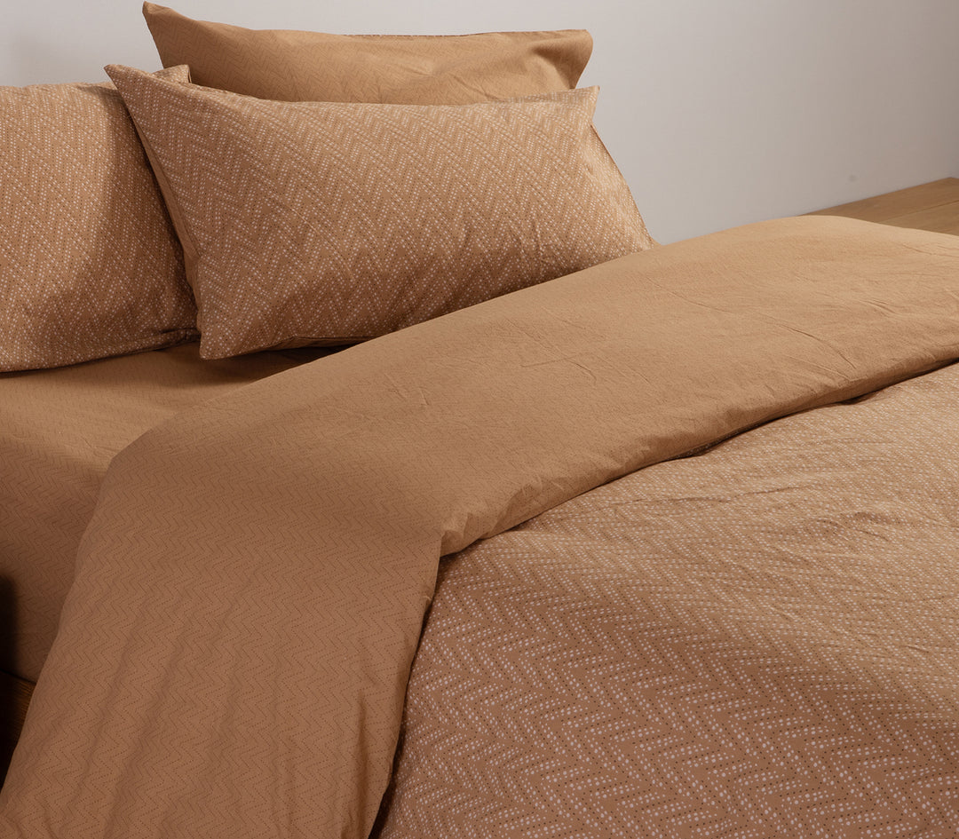 Καφέ σετ σεντονιών με λεπτό ζιγκ-ζαγκ μοτίβο, στρωμένο σε κρεβάτι με μαξιλαροθήκες στο ίδιο σχέδιο.