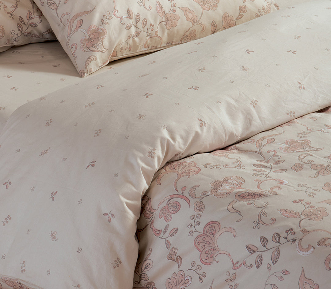 Κρεβάτι με εκρού σετ σεντόνια και ροζ λουλουδάτο σχέδιο, συνδυασμένο με μαξιλαροθήκες στο ίδιο μοτίβο.
