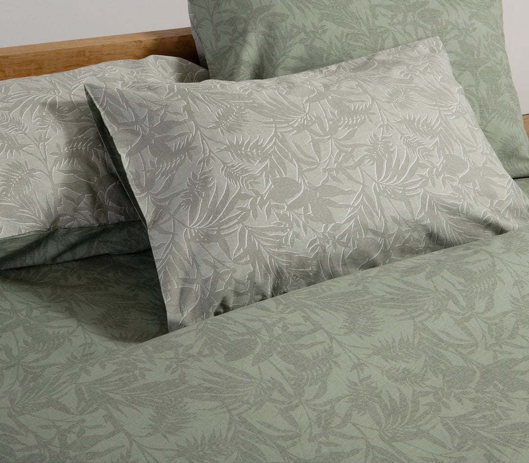 Κοντινή λήψη σε πράσινο σετ σεντονιών με λεπτομέρειες φυλλωτού σχεδίου, συνδυασμένο με μαξιλαροθήκες στο ίδιο μοτίβο.