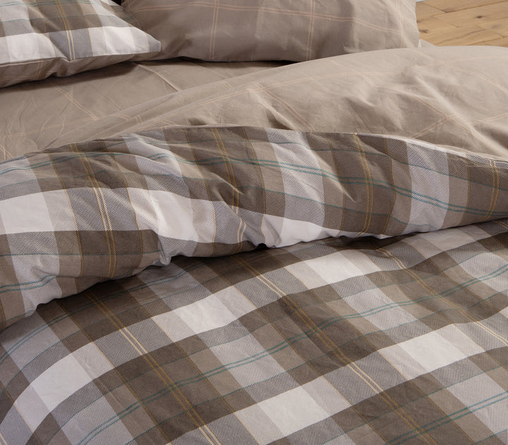 Κρεβάτι με καφέ καρό παπλωματοθήκη και μαξιλαροθήκες σε γήινες αποχρώσεις μπεζ και καφέ.