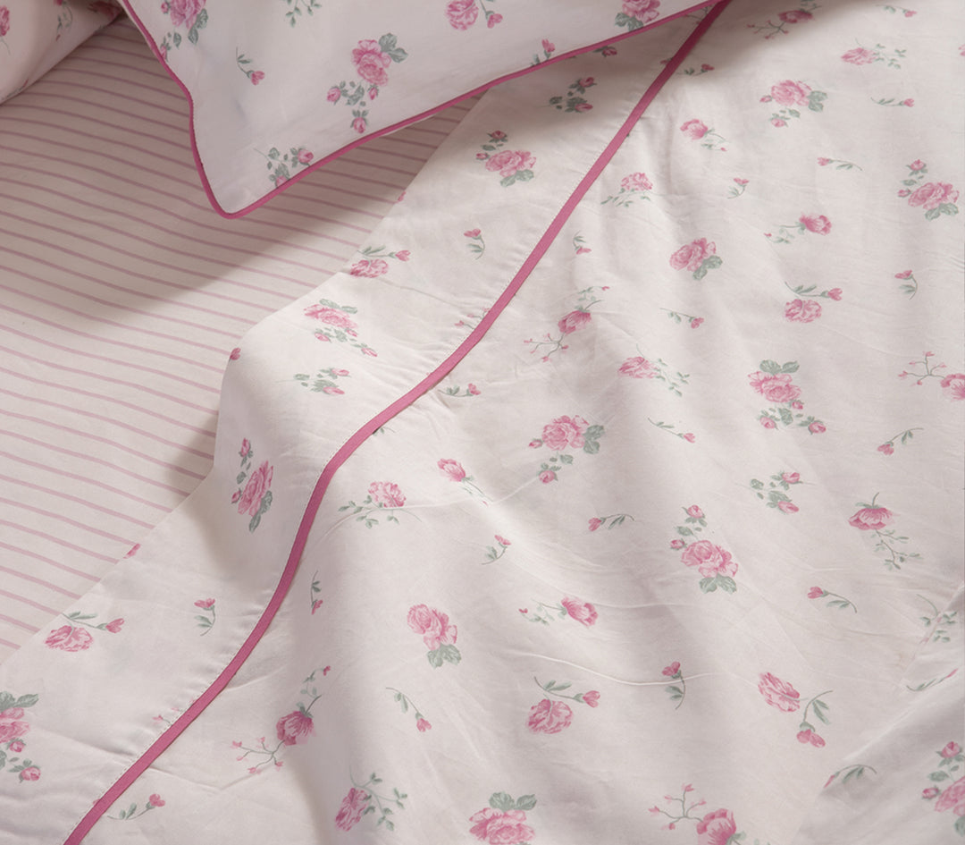 Λεπτομέρεια σετ σεντονιών με λευκή βάση και ροζ λουλούδια, κατωσέντονο με ροζ ρίγες.