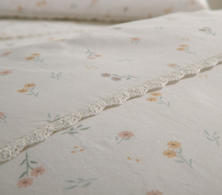 Λεπτομέρεια σετ σεντονιών με λευκή βάση και μικρά λουλούδια σε κίτρινες και πορτοκαλί αποχρώσεις, διακοσμημένο με δαντέλα.