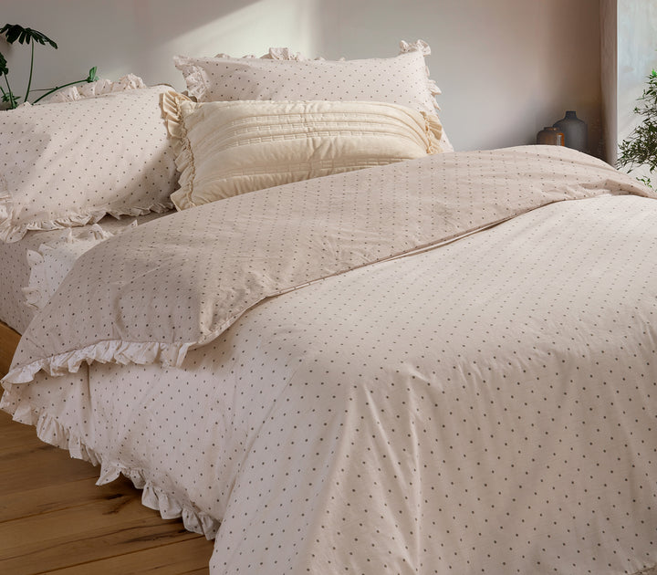 Υπνοδωμάτιο με φυσικό φωτισμό και κρεβάτι στρωμένο με σετ σεντόνια σε μπεζ χρώμα με πουά και βολάν, που αποπνέει κομψότητα και ζεστασιά.