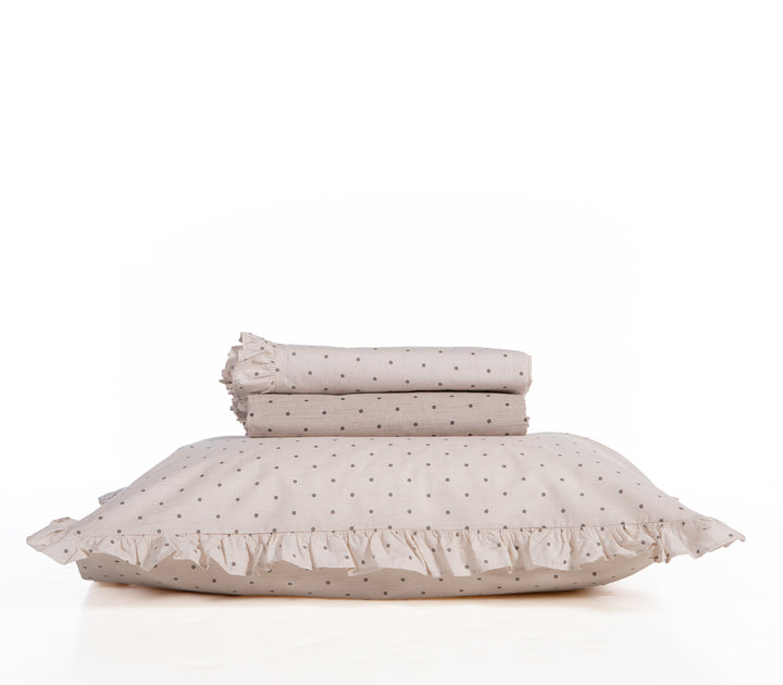 Σετ σεντόνια σε μπεζ φόντο με μαύρα πουά και διακοσμητικό βολάν, διπλωμένα τακτοποιημένα πάνω σε μαξιλάρι, σε λευκό φόντο.