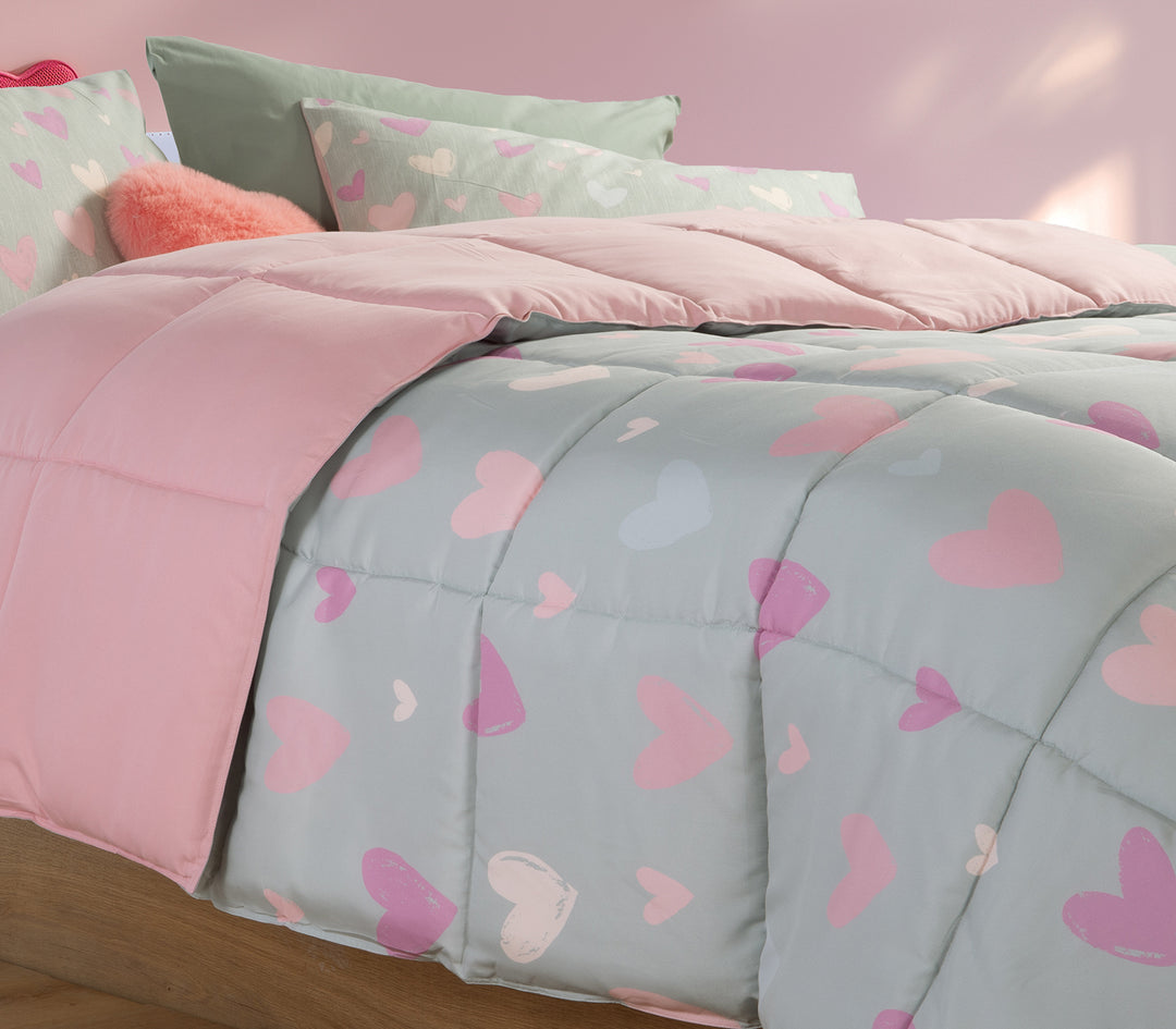 Κοντινή λήψη παιδικού δωματίου με πάπλωμα σε μέντα χρώμα και σχέδιο καρδιές με αντίστοιχα μαξιλάρια όπως και διακοσμητικό μαξιλάρι κόκκινο καρδιά.