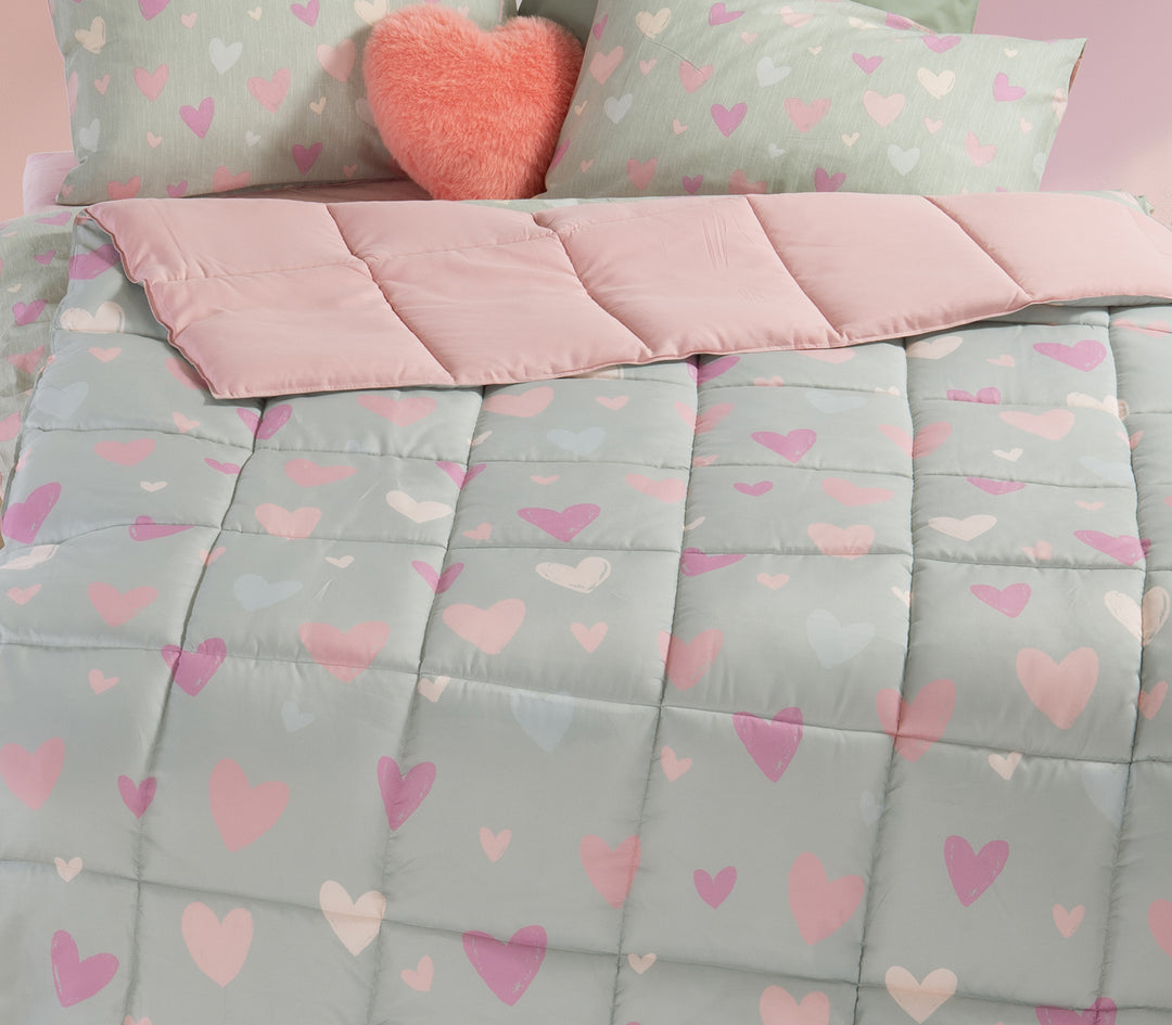 Κοντινή εικόνα παιδικού δωματίου με πάπλωμα σε μέντα χρώμα και σχέδιο καρδιές με γυρισμένο το πάνω μέρος και  αντίστοιχα μαξιλάρια όπως και διακοσμητικό μαξιλάρι κόκκινο καρδιά.