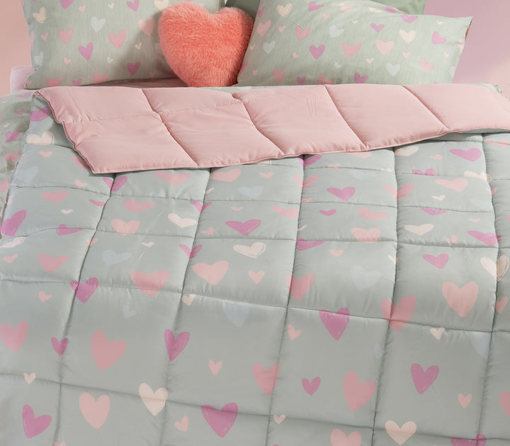 Κοντινή εικόνα παιδικού δωματίου με πάπλωμα σε μέντα χρώμα και σχέδιο καρδιές με γυρισμένο το πάνω μέρος και  αντίστοιχα μαξιλάρια όπως και διακοσμητικό μαξιλάρι κόκκινο καρδιά.