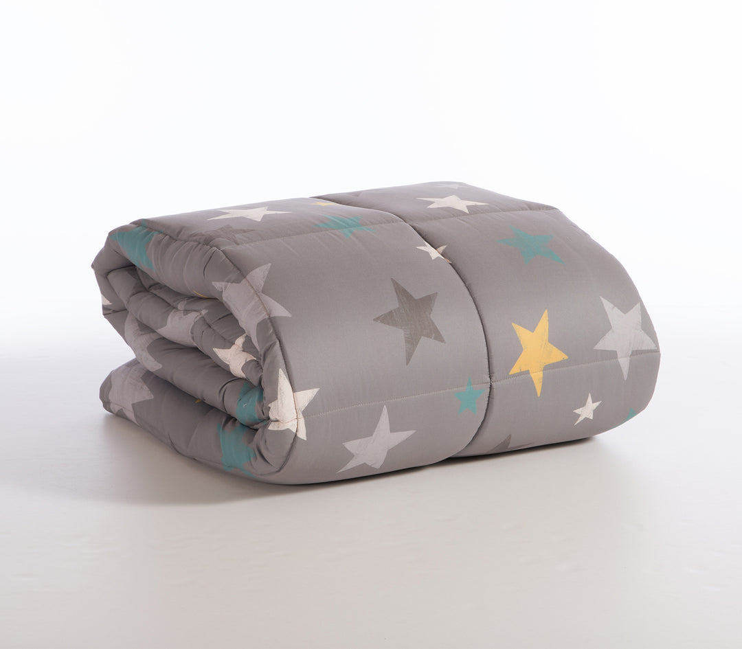 Διπλωμένο Παιδικό πάπλωμα σε γκρι φόντο με πολύχρωμα αστέρια σε αποχρώσεις κίτρινου, γαλάζιου, λευκού και σκούρου γκρι.