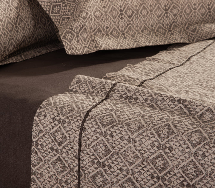 Κοντινή λήψη καφέ και μπεζ σεντονιών με γεωμετρικό σχέδιο και καφέ μονόχρωμο κατωσέντονο