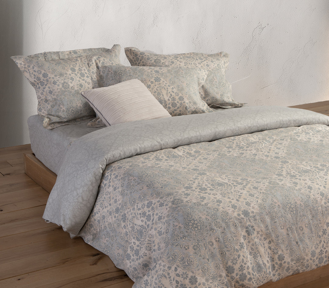 Κρεβάτι με σετ σεντόνια σε γκρι και εκρού αποχρώσεις, διακοσμημένο με διακριτικό λουλουδάτο μοτίβο.