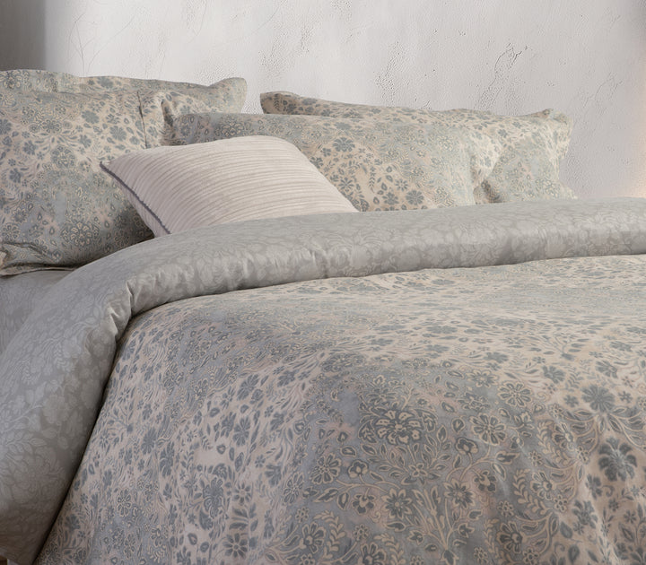 Κρεβάτι με λευκά είδη σε γκρι και εκρού τόνους με μοτίβο λουλουδιών σε minimal υπνοδωμάτιο.