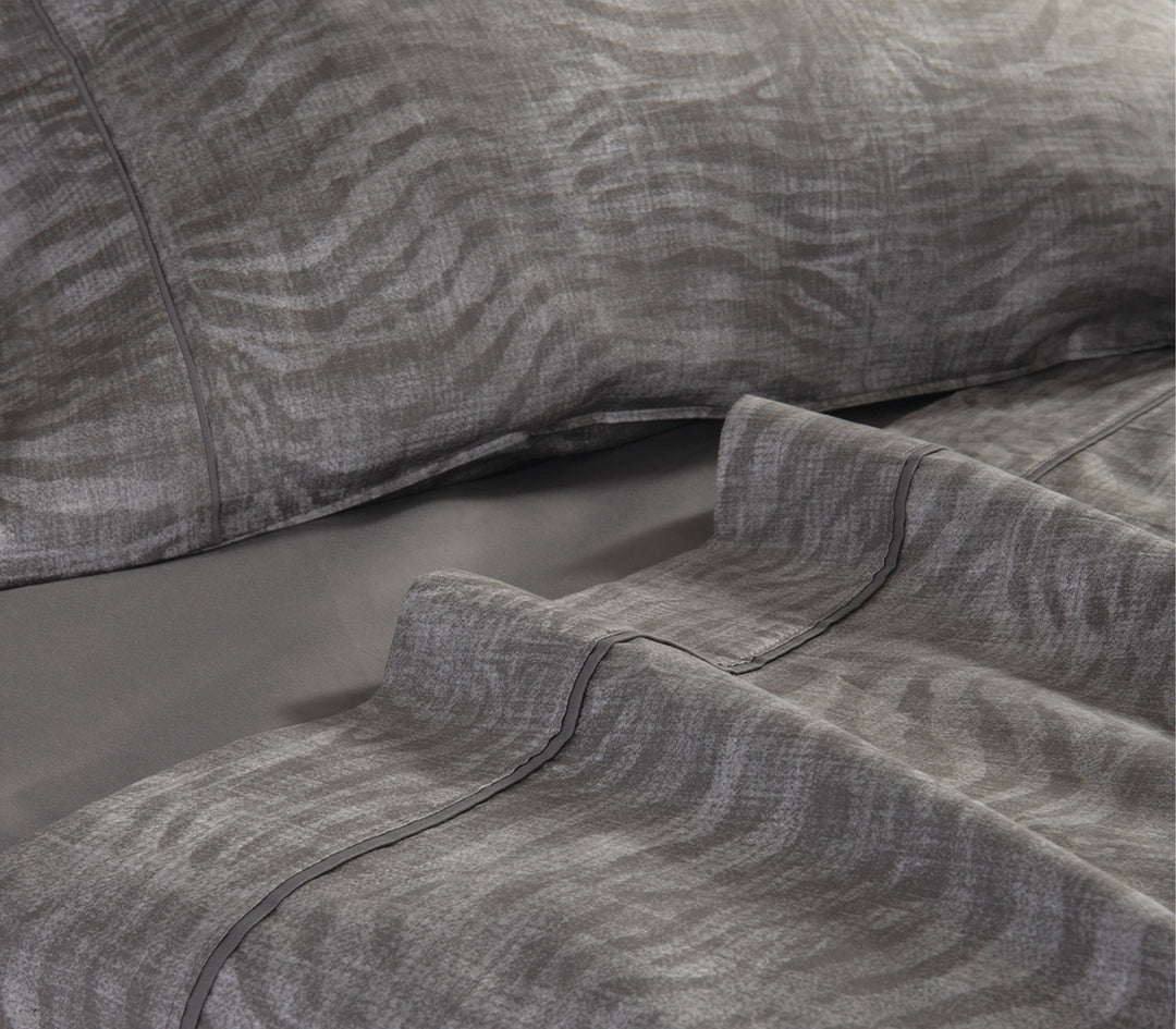 Κοντινή λήψη γκρι σεντονιών με animal print σχέδιο σε στρωμένο κρεβάτι.