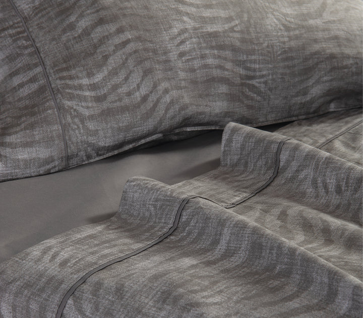 Κοντινή λήψη γκρι σεντονιών με animal print σχέδιο σε στρωμένο κρεβάτι.