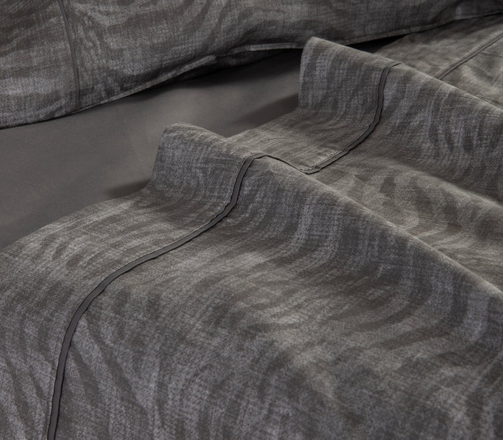 Γκρι σεντόνι με διακριτικό animal print σχέδιο σε κοντινή λήψη πάνω στο κρεβάτι.