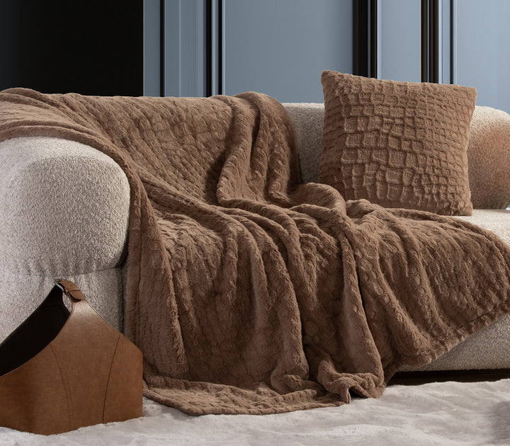 Καφέ γούνινη κουβέρτα με μαξιλάρι σε ίδιο σχέδιο πάνω σε μπεζ καναπέ σαλονιού.