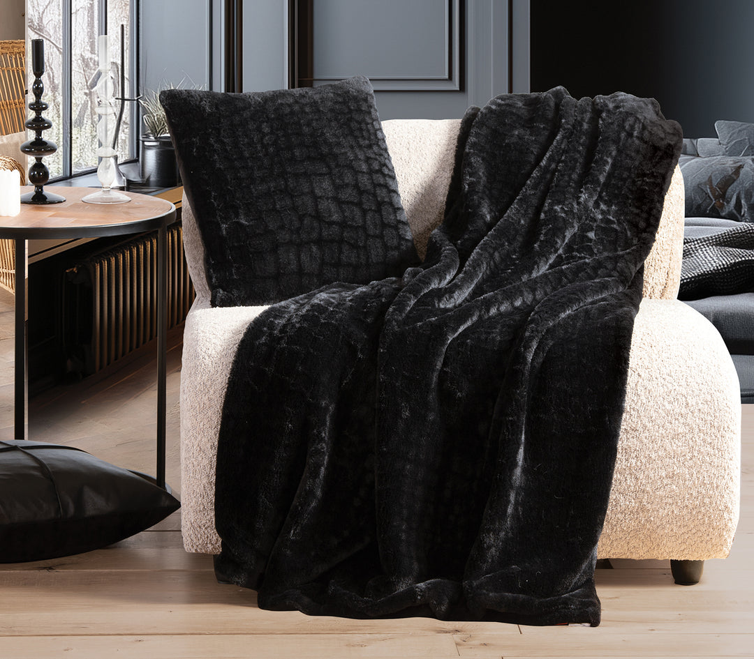Μαύρη γούνινη κουβέρτα με ανάγλυφο σχέδιο και μαξιλάρι σε μπεζ πολυθρόνα.