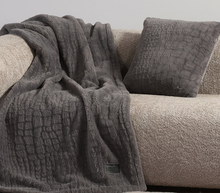 Γκρι κουβέρτα με μαξιλάρι σε ίδια υφή επάνω σε μπεζ καναπέ.
