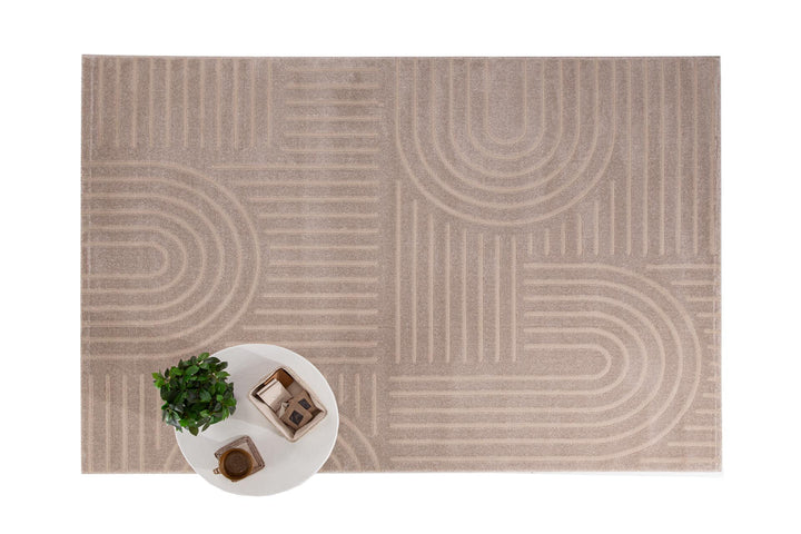 Μπεζ χαλί Organic Royal Carpet με γεωμετρικές γραμμές και καμπύλες, πλαισιωμένο από λευκό στρογγυλό τραπέζι με φυτό και κουτί οργάνωσης.