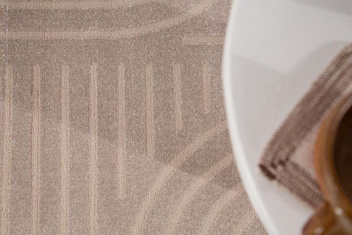 Κοντινή λήψη μπεζ χαλιού Organic Royal Carpet με λεπτομέρεια καμπυλωτού γεωμετρικού μοτίβου δίπλα σε τραπεζάκι με διακόσμηση.