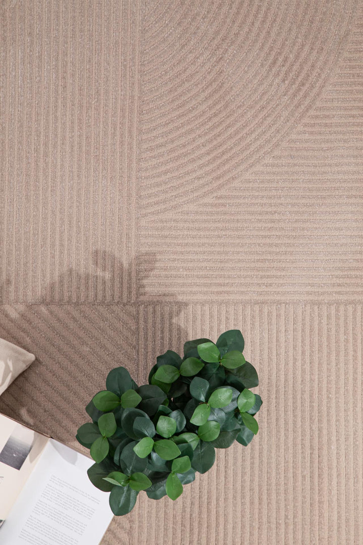 Μοντέρνο χαλί Organic Royal Carpet σε μπεζ τόνους με γεωμετρικό σχέδιο, διακοσμημένο με πράσινο φυτό και ανοιχτό βιβλίο.
