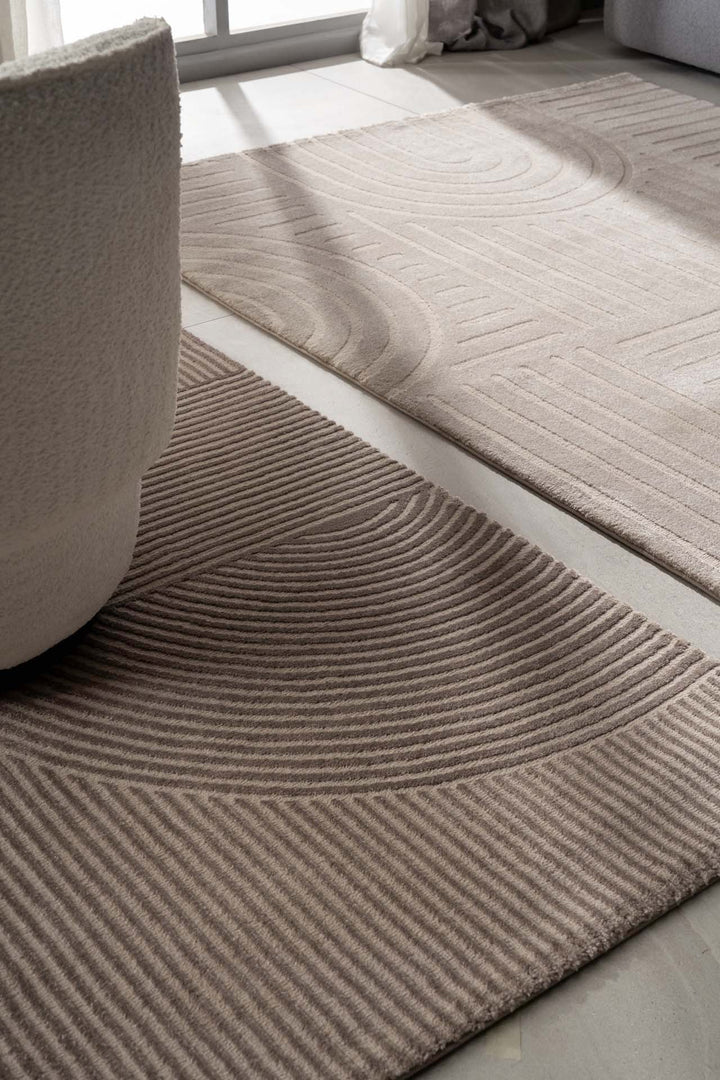 Χαλί Organic Royal Carpet σε μπεζ και εκρού τόνους με ανάγλυφο σχέδιο γραμμών, τοποθετημένο σε σαλόνι δίπλα σε πολυθρόνα και παράθυρο.