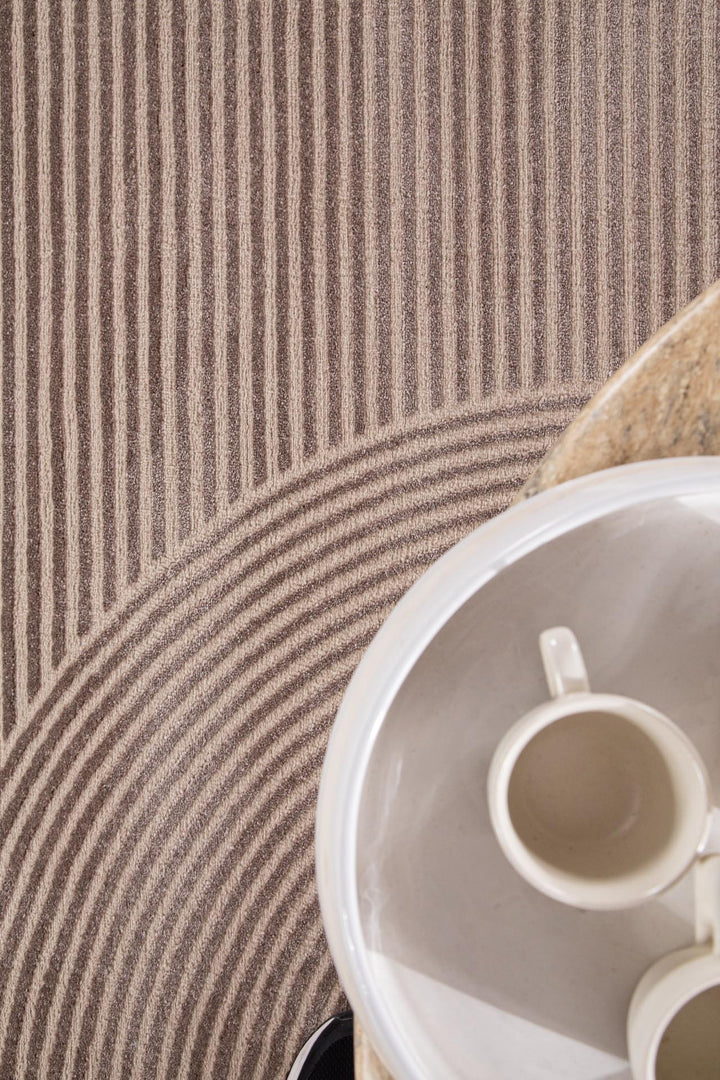 Κοντινό σε μοντέρνο χαλί Organic της Royal Carpet σε μπεζ απόχρωση με γεωμετρικό μοτίβο από γραμμές, δίπλα σε λευκή κούπα καφέ.